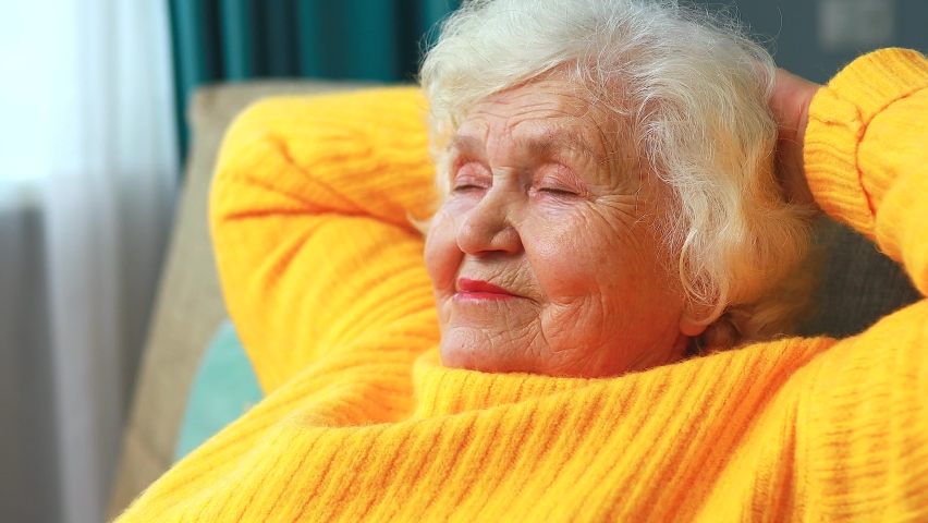 mature woman dreaming, thinking about good future sitting on sofa in living room