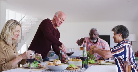 Diverse senior couples sitting by a table drinking wine and eating dinner. health fitness wellbeing at senior care home.