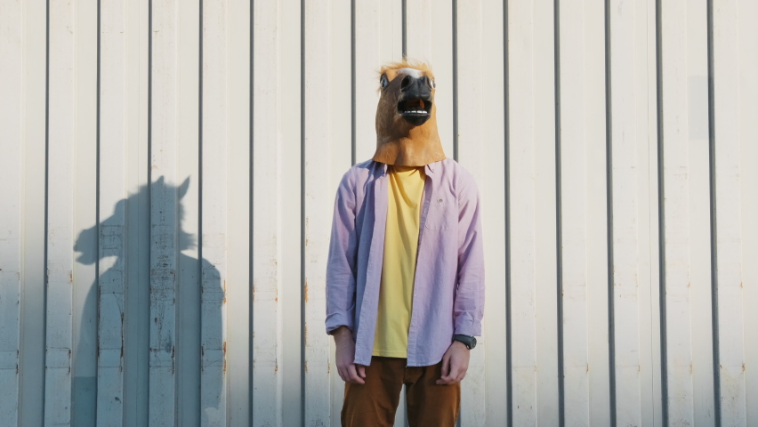 Dancing Funny Young Man in a Horse Mask Rhythmically Moving his arms Up on a Gray Background in the Street Slow Motion in Sunny Day. Crazy fun dancing Hipster. Happiness Holidays. Face Horse