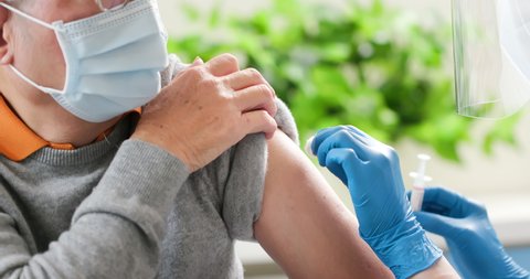 close up of asian female doctor wearing gloves and isolation mask is making a COVID-19 vaccination in the shoulder of senior male patient at hospital