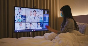 Telemedicine concept - asian woman patient lying on bed has video call with doctors team by big screen TV in a hospital ward or at home