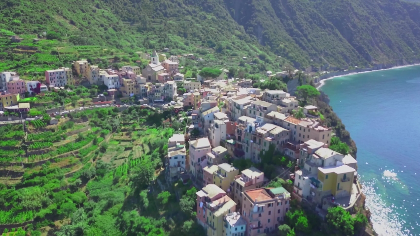 Flight by a drone of Corniglia village one of Cinque Terre coast of Italy in region of Liguria, Italy.Houses,plantation of grapes on the edge of cliffs,azure seawater and rocks by shore,top view. 4K