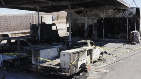 Burnt out cars and trucks behind police tape at scene of gas station fire