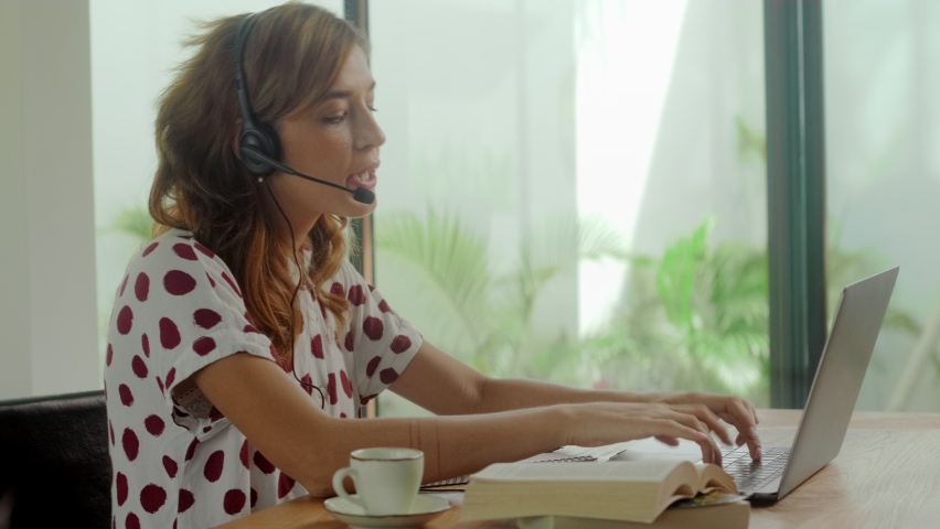 Female call center worker sitting desk focus on customer service member girl in headset looks at laptop screen write in notebook talk with client provide insurance information sell company product Royalty-Free Stock Footage #1066221241