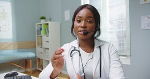 African female doctor wear headset make online video call consult patient. Afro american black woman therapist videoconferencing talking to camera in remote chat. Telemedicine, telehealth. Webcam view