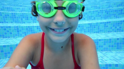 Happy girl in goggles swim underwater in pool. Close up