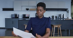 African american businesswoman having video chat going through paperwork and listening in workplace kitchen. business communication workiung online in modern office.