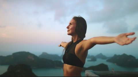 Bokeh Thailand's sunset: woman rise up hands at seascape with green small hilly islands in National Marine Park. Pretty girl with long hair looks on Thai sun setting. Cinematic footage shot in 4K, UHD