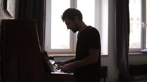 Bearded man professionally play the piano at home against window
