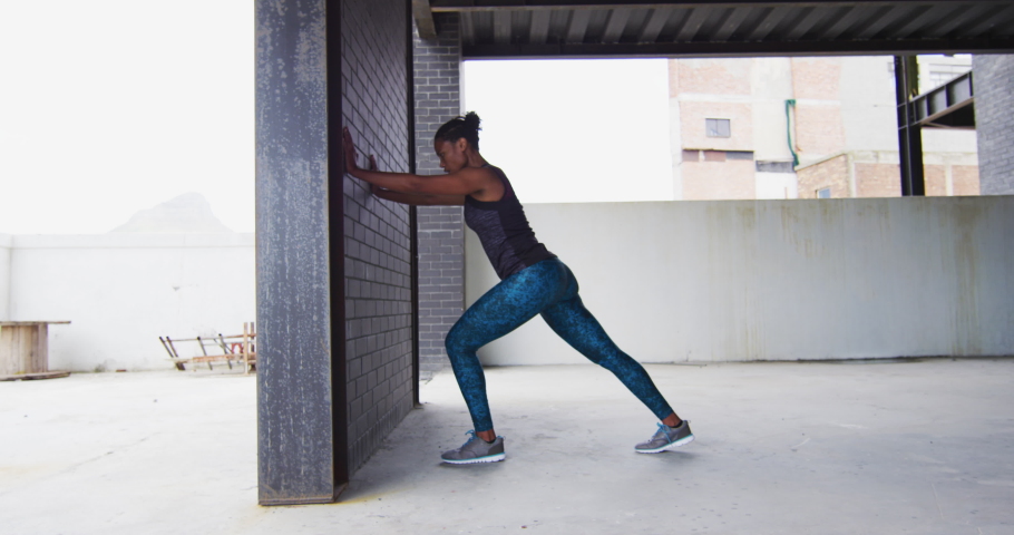 African american woman stretching leaning on a wall in an empty urban building. urban fitness and healthy lifetyle.