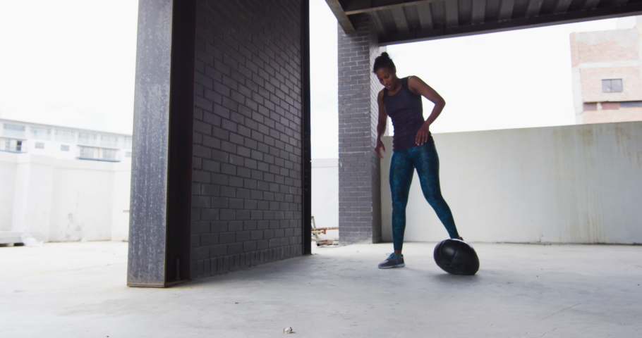 African american woman resting after exercising with medicine ball in an empty urban building. urban fitness and healthy lifetyle.