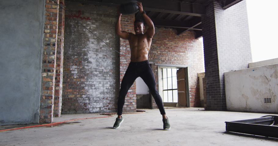 Shirtless african american man exercising with medicine ball in an empty urban building. urban fitness and healthy lifetyle.