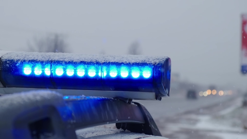 Blue lights of a police car flash against the snow in the evening. Close up shot