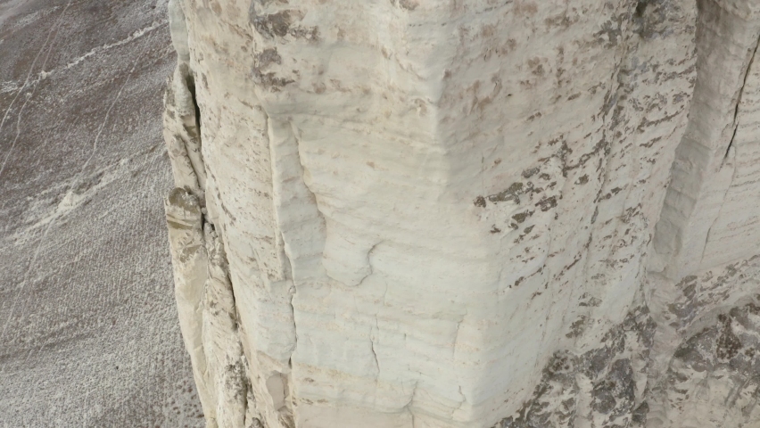 Aerial shooting upwards rocky texture. Amazing view from above tourist couple standing on observation deck on mountain peak white cliff.
