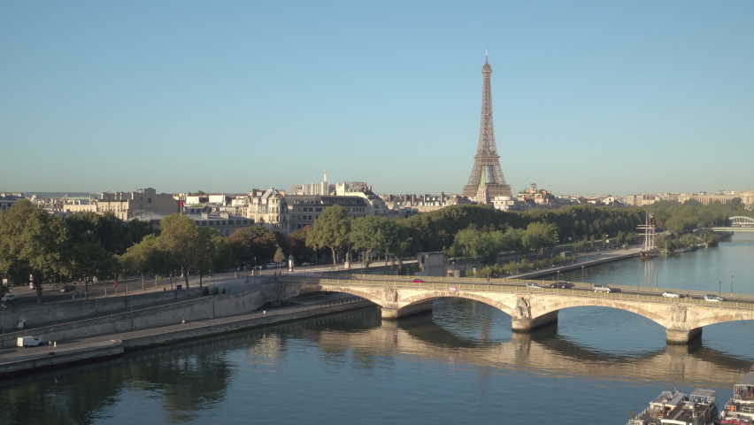 Aerial elevation from the docks of the Seine river in Paris toward the Eiffel Tower at sunrise, bridge with traffic in front. Ending view on the Eiffel tower in the middle of Paris cityscape, 4K Royalty-Free Stock Footage #1066237669