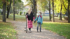 Wide shot of relaxed Caucasian mother and son in coronavirus face masks walking in autumn park with electric scooter and talking. Portrait of young woman and cute boy strolling outdoors on pandemic. - Powered by Shutterstock - Get 15% off with code: PIKWIZARD15