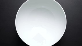 chopped vegetables fall into a white salad bowl. white plate on black background. High quality 4k footage