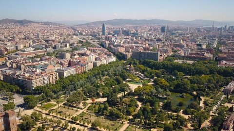 The drone flies forwards above Parc de la Ciutadella and the city centre all around and Torre Agbar and Torre Glories and big hills in the background in Barcelona Spain Aerial Drone Footage 4K