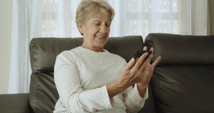 A senior retirement woman with short cut light brown hair holds her phone and enjoy social media on the Internet happily.