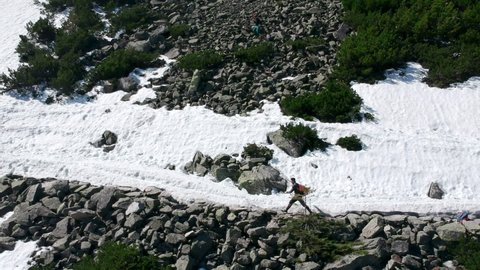 Aerial footage of a guy running in the snowy mountains with backpack (stones, bushes, frost, winter)