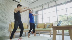 Asian couple doing exercise by follow video instruction. Stay home relaxing in living room. Togetherness concept.