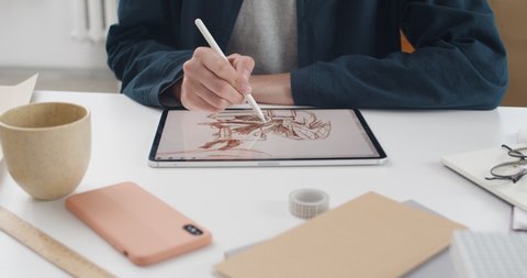 Lviv, Ukraine - May 28, 2020: Crop view of illustrator hands drawing picture on tablet screen. Talanted graphic designer using digital pad and stylus while sitting and working on project. Indoors.