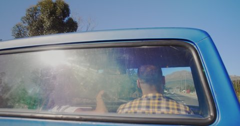 Rear view of a young mixed race couple driving during a road trip, seen through the rear window of their pick-up truck
