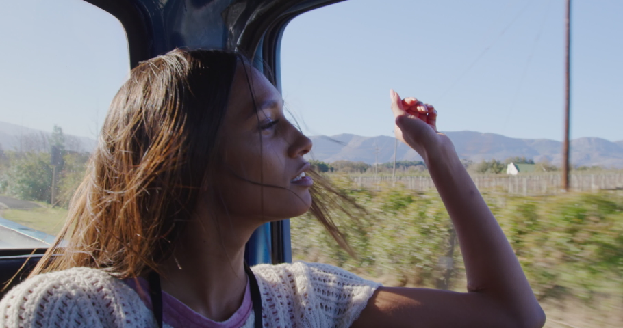 Side view of a young mixed race woman sitting in a pick-up truck, looking out of a window during a road trip