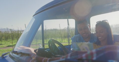 Front view of a young mixed race couple sitting in their pick-up truck, smiling and reading a map during a road trip