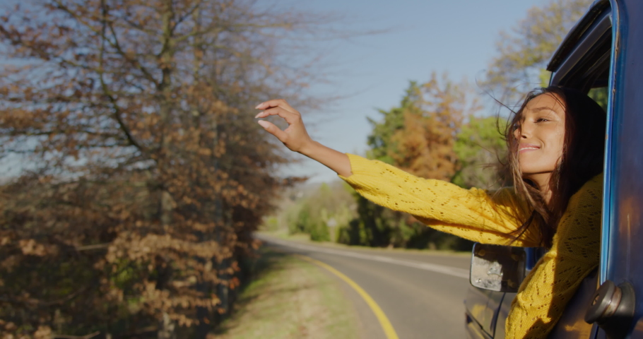 Front view of a young mixed race woman sitting in a pick-up truck, leaning out of a window with her arm out and smiling during a road trip