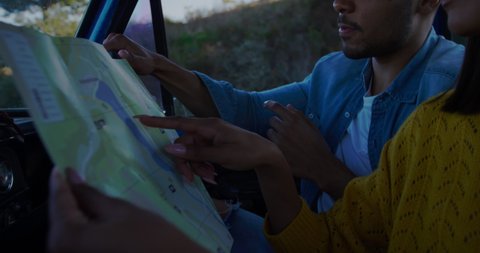 Close up side view of a young mixed race couple sitting in their pick-up truck, reading a map during a road trip