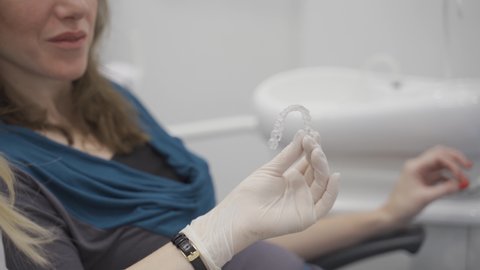 Close up on hand of orthodontist holding invisible retainer for teeth alignment. In clinic shows patient modern dental technology - removable transparent plastic aligners or Invisalign use and benefit