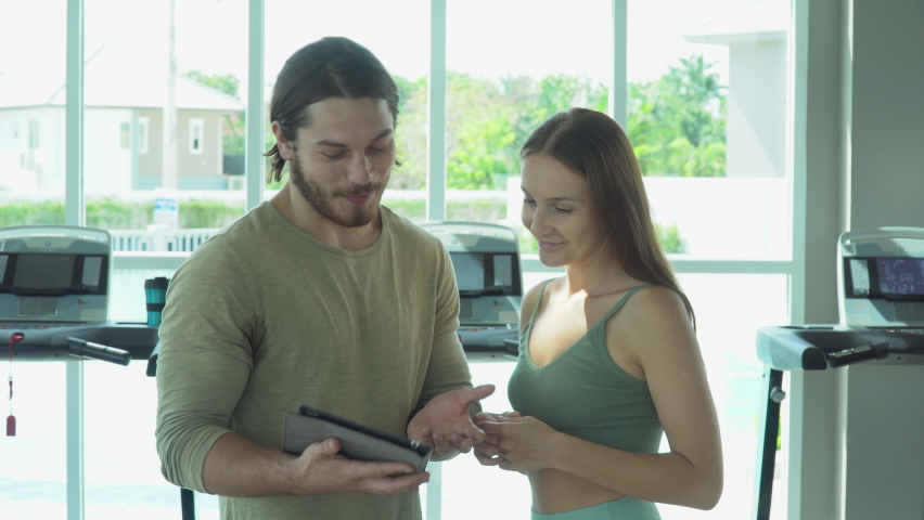 group of fitness woman and sport man conversation together with digital tablet after exercising class in the gym. Group of young fit people standing talking and relaxing in sport club after workout 