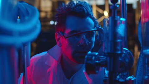 Close up of crazy chemist making experiment using large equipment in industrial laboratory. Man scientist in plastic goggles and lab coat controlling chemical process 
