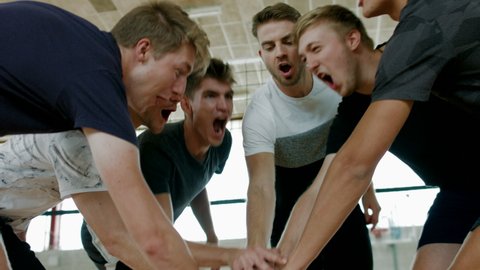 A group of young volleyball male players cheering and putting hands together before start playing the game.