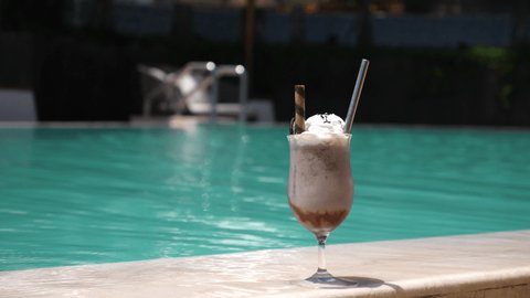 Hand taking a glass of vegan chocolate milkshake from the edge of swimming pool. Enjoying holidays 