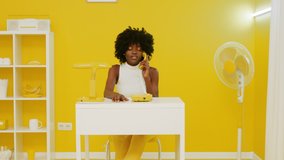 Pretty African woman, art manager, is sitting at desk and talking on retro phone, in beautiful yellow-and-white office, creative video concept, Slow motion.