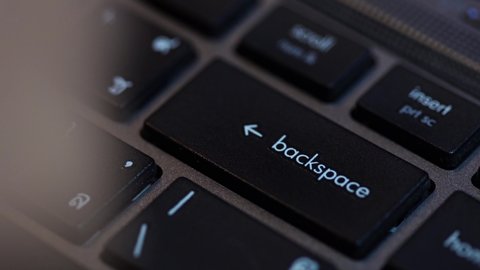 Human fingers press the Backspace key on the computer keyboard.