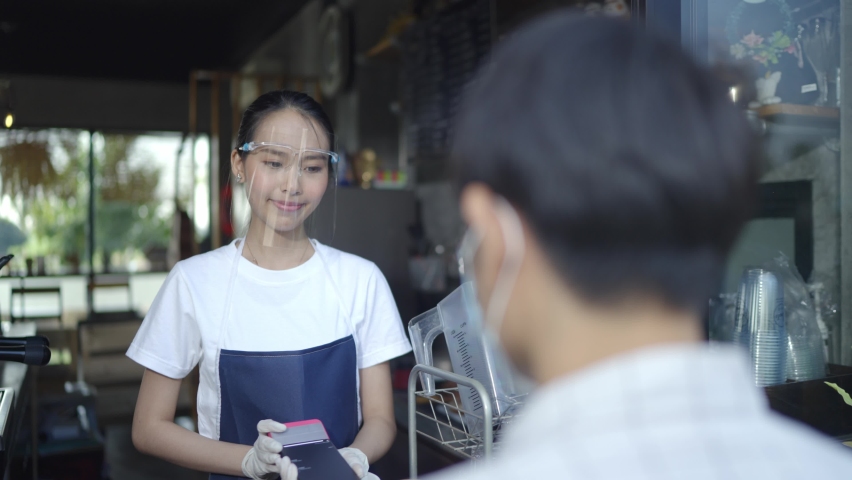 VDO Slow-motion.Female coffee shop staff wearing face shield serving coffee ordered takeaway. By making payment via a smartphone scan.New Normal Concetp