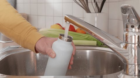 Man fills up reusable water bottle in the kitchen. Sustainable lifestyle concept, people using reusable bottles, plastic free environment