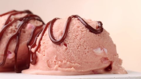 closeup of two pink ice cream scoops and flowing chocolate sauce turning on beige background