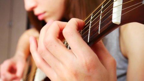 A young beautiful woman plays acoustic guitar at home close-up