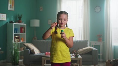 Portrait of small girl with two braids, in yellow T-shirt, smiling at camera and blowing bubbles, open-minded kid that has happy childhood, Foreground, Slow motion.