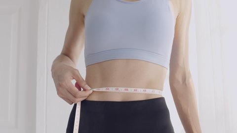 Cloe up shot of slim woman in sportswear measuring her waist with measurement tape.