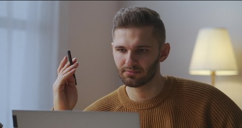 man is communicating by video call on laptop, listening and answering, portrait in room, working from home