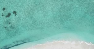 A drone rises over a beach in the Maldives, aerial view and waves wash ashore.	