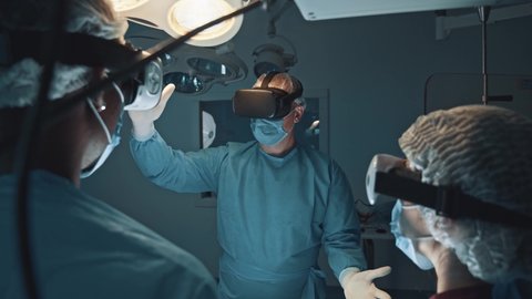 Futuristic medical diagnose through virtual reality glasses simulator and interactive screen. Doctor and his team disease diagnosis patient health on 3D VR headset in hospital surgical room. Medicine