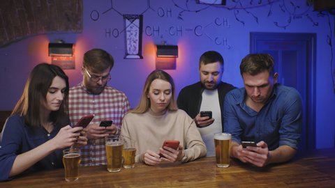 Friends in pub at bar counter with beer look at their phones. Social life
