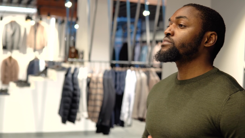 A young elegant african american man wearing olive green suit is standing on a sofa in a showroom or boutique