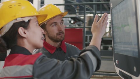 Slowmo close-up of couple of multi-ethnic engineers working with touchscreen monitor of modern machine equipment at industrial factory
